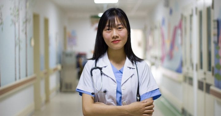 a doctor stands in a hospital with her arms crossed